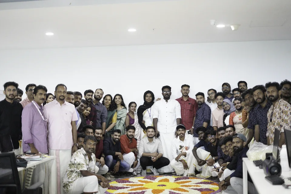 A group gathered around a colourful floral pookalam for Onam